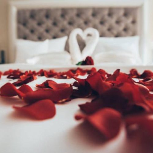A bed covered with rose petals, with swans made of towels that form a heart. Honeymoon and wedding concept. Dating and Valentine's day.